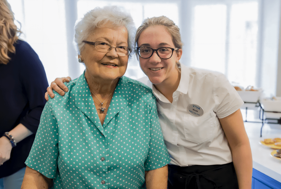 A young uniformed Viva staff member poses with an elderly lady, her arm around her shoulder.