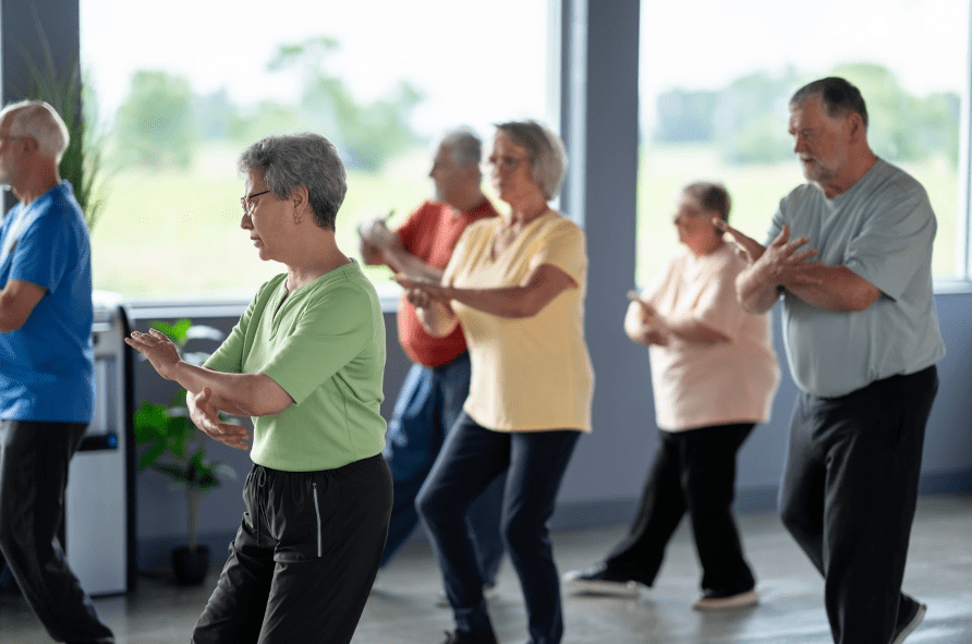 Seniors participating in a group Tai Chi class in a bright fitness room.