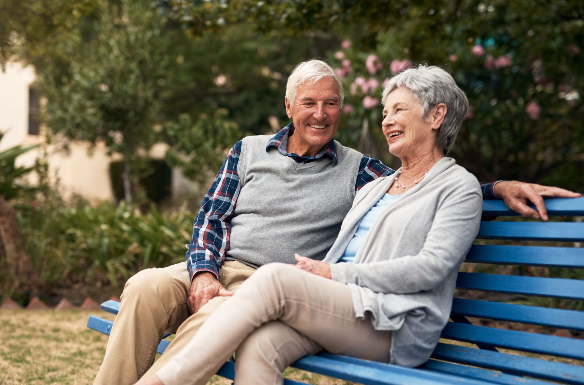 Smiling senior couple sitting on a park bench, enjoying a peaceful moment together outdoors.