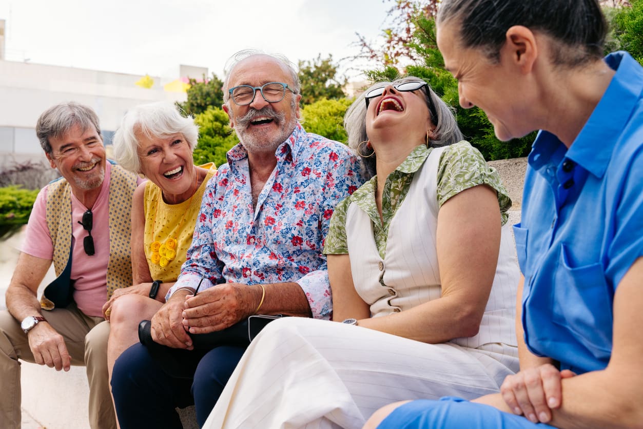 Group of seniors laughing together outside in a retirement community garden.