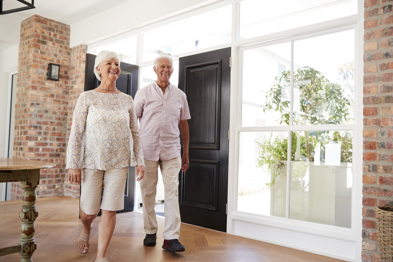 Smiling senior couple entering a bright and welcoming retirement community lobby.