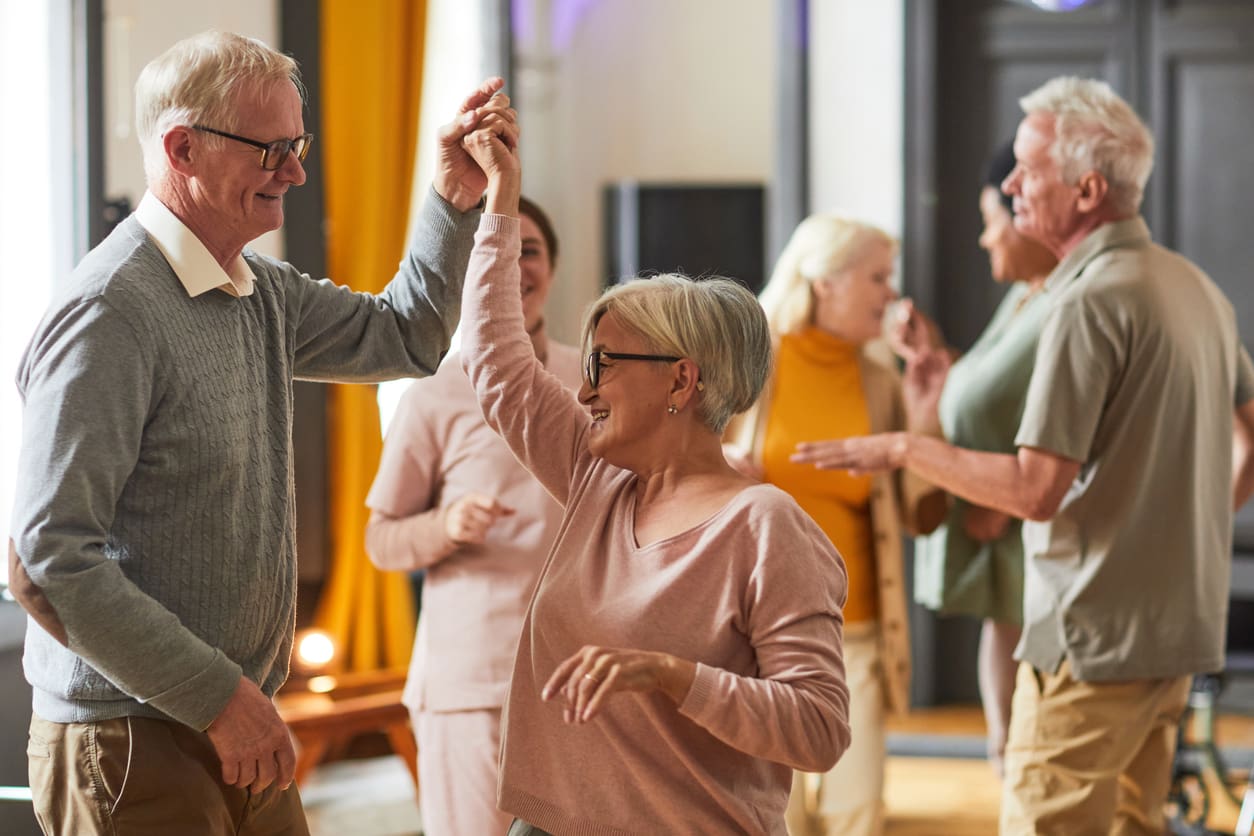 Happy seniors dancing and socializing at a lively community event, smiling and enjoying each other's company, highlighting the vibrant lifestyle of a retirement community.