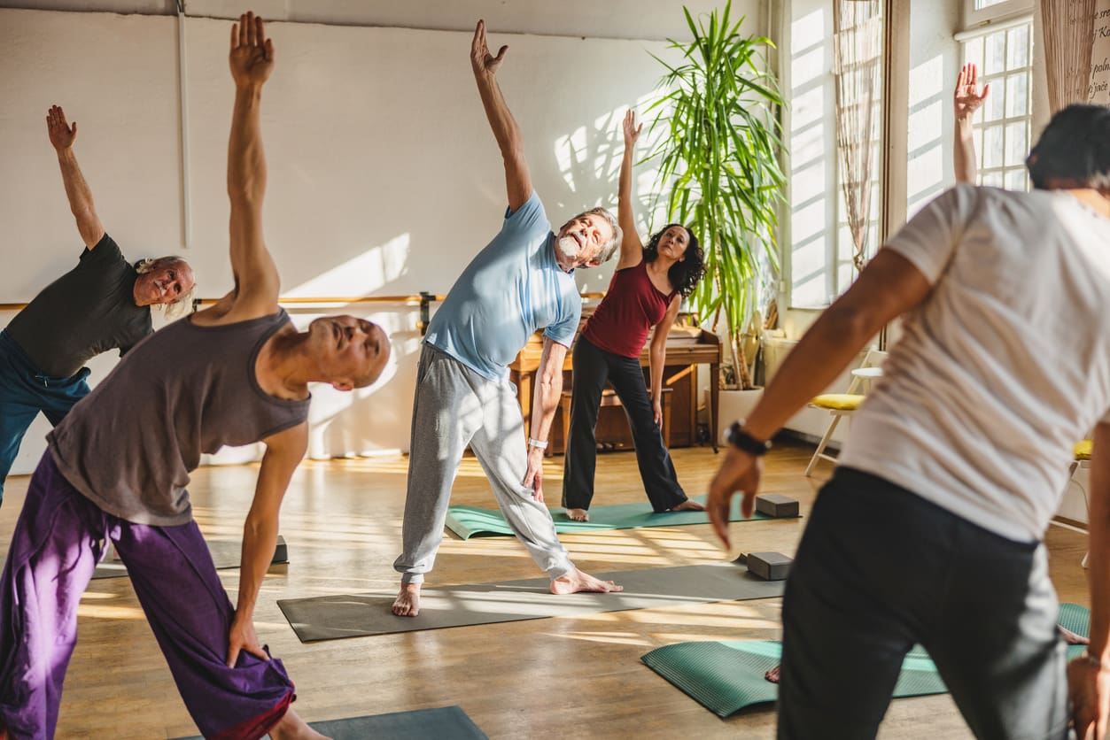 A group of older adults participate in a yoga class in a bright, modern community space, promoting wellness and social engagement as part of retirement community living.