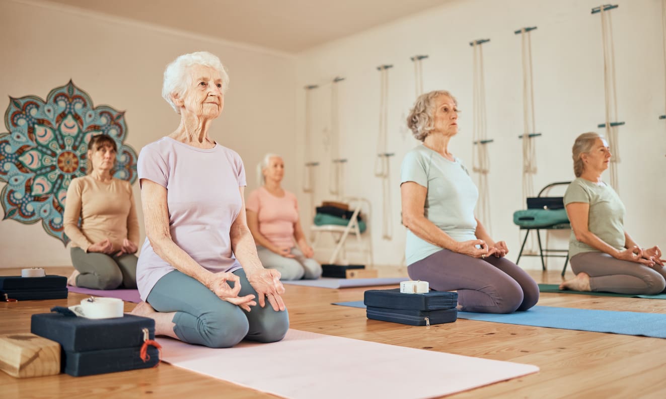 Group of senior women participating in a wellness yoga class in a retirement community fitness studio.