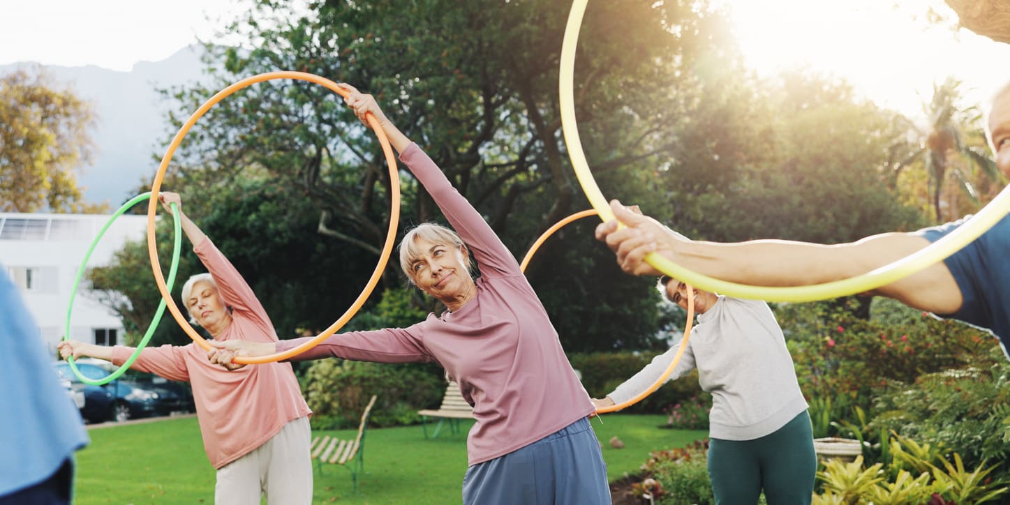 Active older adults stretching with fitness hoops during an outdoor exercise class at a retirement community.