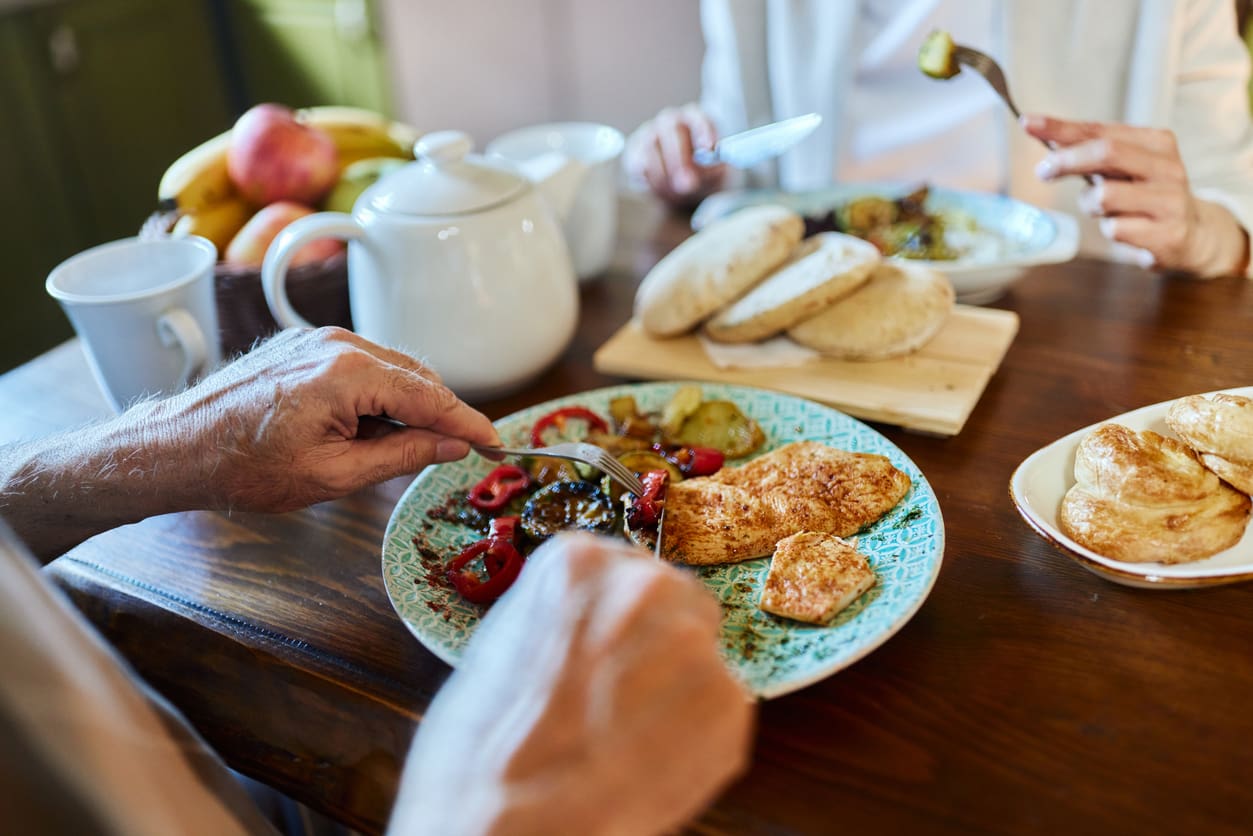 Older couple sharing a freshly prepared meal together in a bright dining room, symbolizing nutritious and joyful dining.