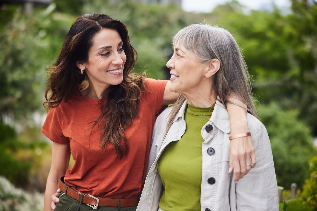 Smiling older woman walking outdoors with her adult daughter, both relaxed and happy after her move to a retirement community.