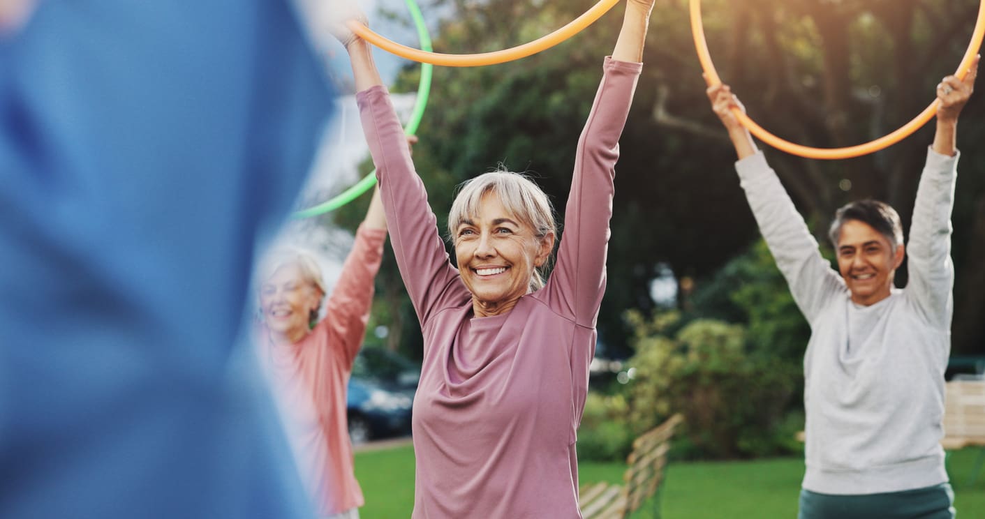 Smiling seniors enjoying an outdoor group fitness class with colourful hoops at a retirement residence.