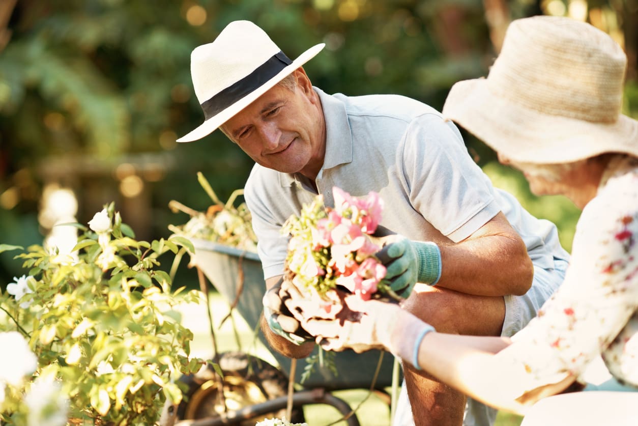 Two older adults planting flowers together in a garden as part of an active retirement community lifestyle.