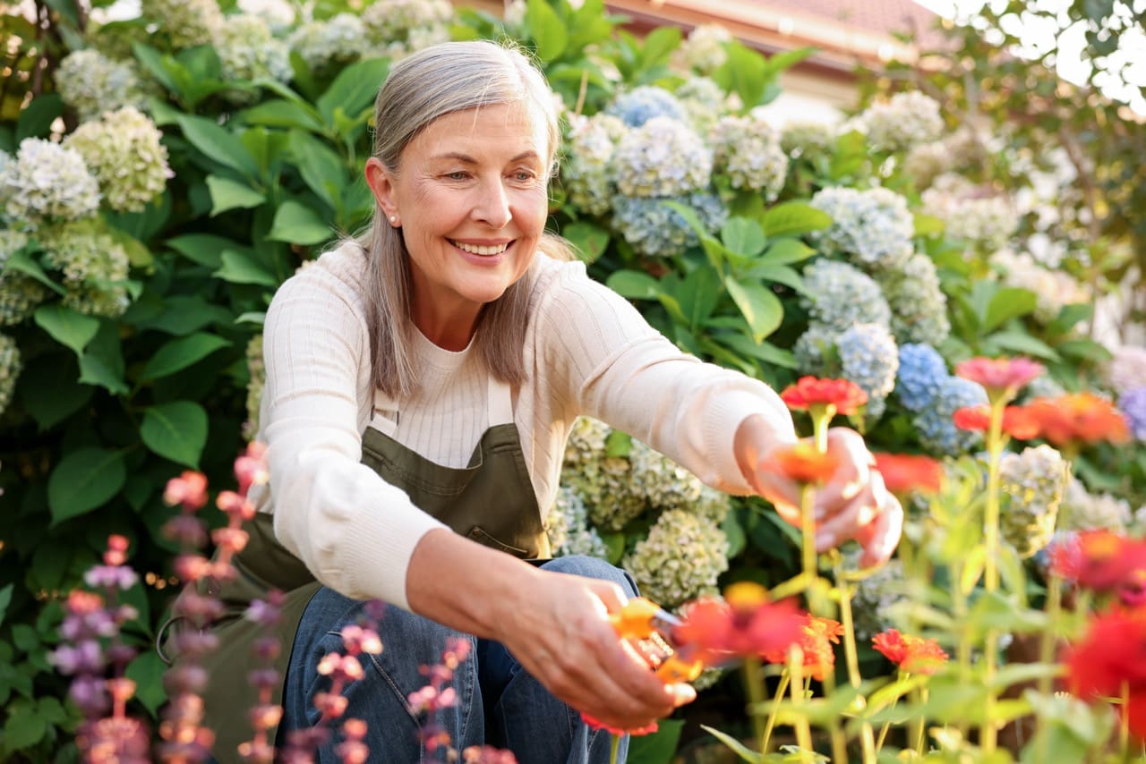 Senior woman pruning flowers outdoors in a Mississauga retirement community garden.